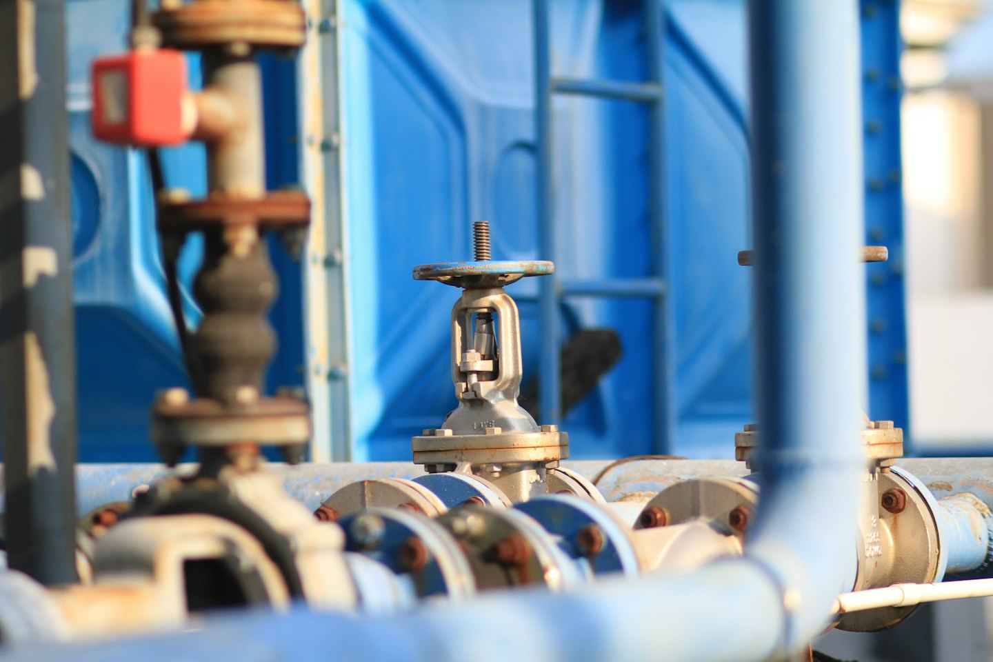 Industrial pipes and a weathered blue gate valve outdoors.