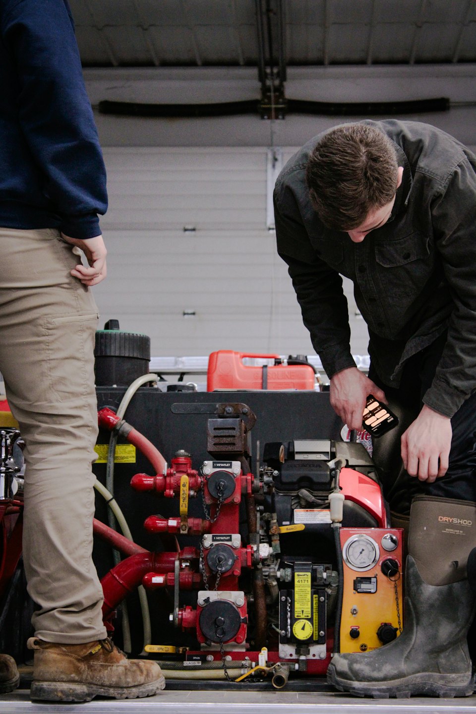 Men inspecting complex mechanical equipment with red hoses and gauges.